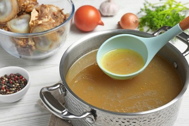 Photo of Delicious homemade bone broth and ingredients on white wooden table, closeup view