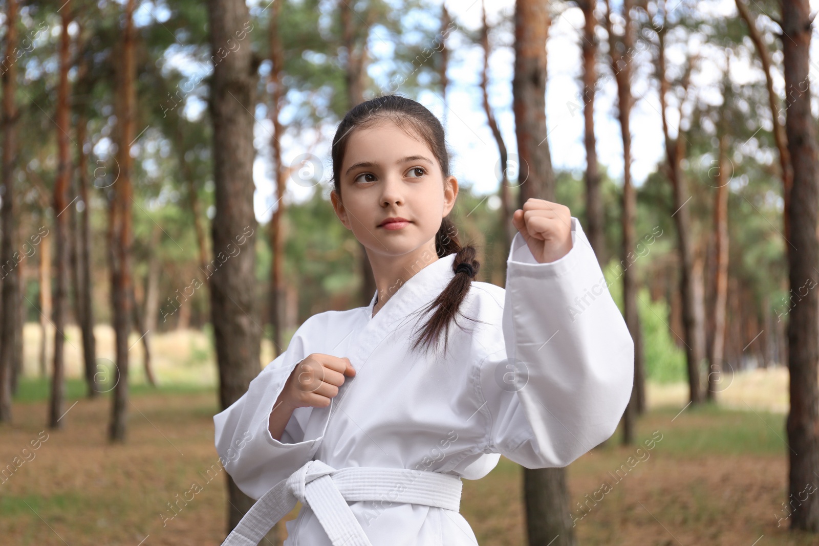 Photo of Cute little girl in kimono practicing karate in forest