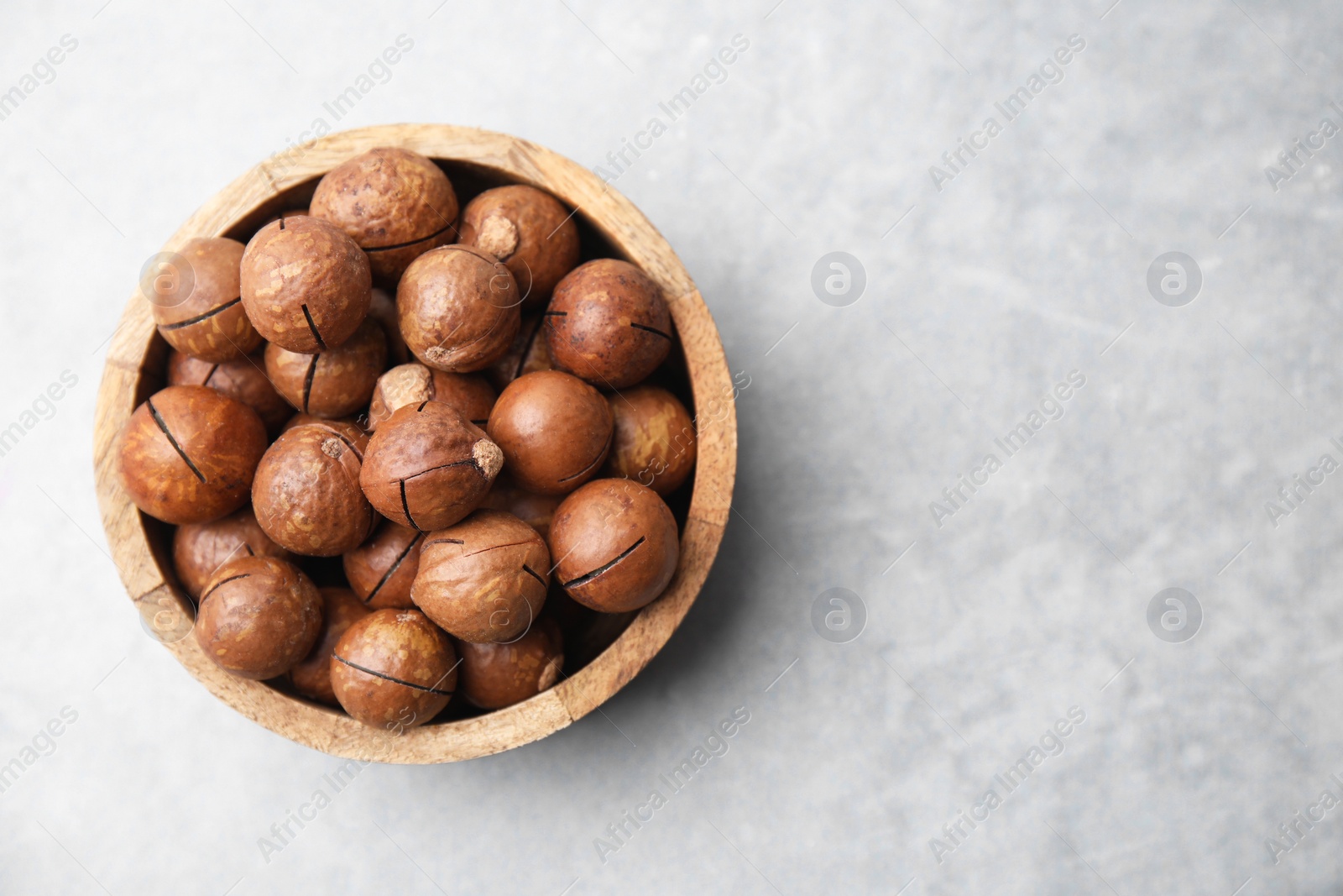 Photo of Delicious macadamia nuts in bowl on light grey table, top view. Space for text