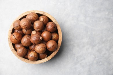 Delicious macadamia nuts in bowl on light grey table, top view. Space for text