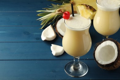 Photo of Tasty Pina Colada cocktails and ingredients on blue wooden table, space for text