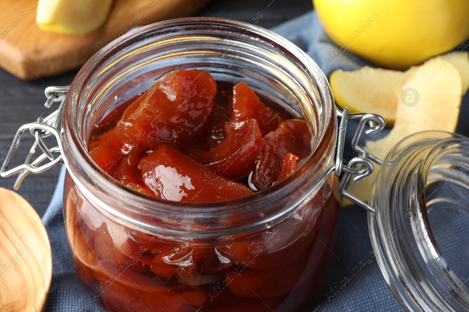 Photo of Quince jam in glass jar and fresh raw fruits on table, closeup