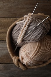 Soft colorful yarns, knitting and metal needles on wooden table, top view