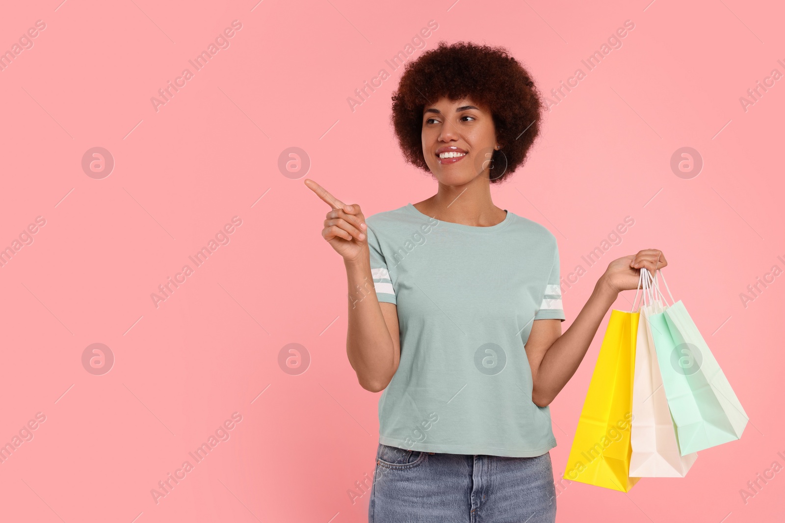 Photo of Happy young woman with shopping bags pointing at something on pink background. Space for text