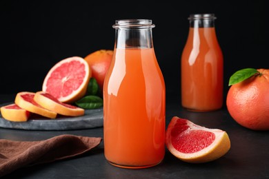 Photo of Tasty freshly made grapefruit juice and fruit on black table