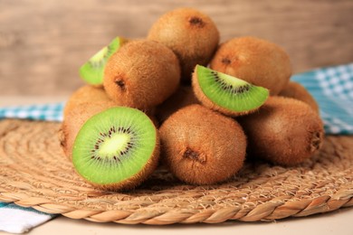 Heap of whole and cut fresh kiwis on wicker mat, closeup