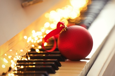 Photo of Beautiful red bauble and fairy lights on piano keys, closeup. Christmas music