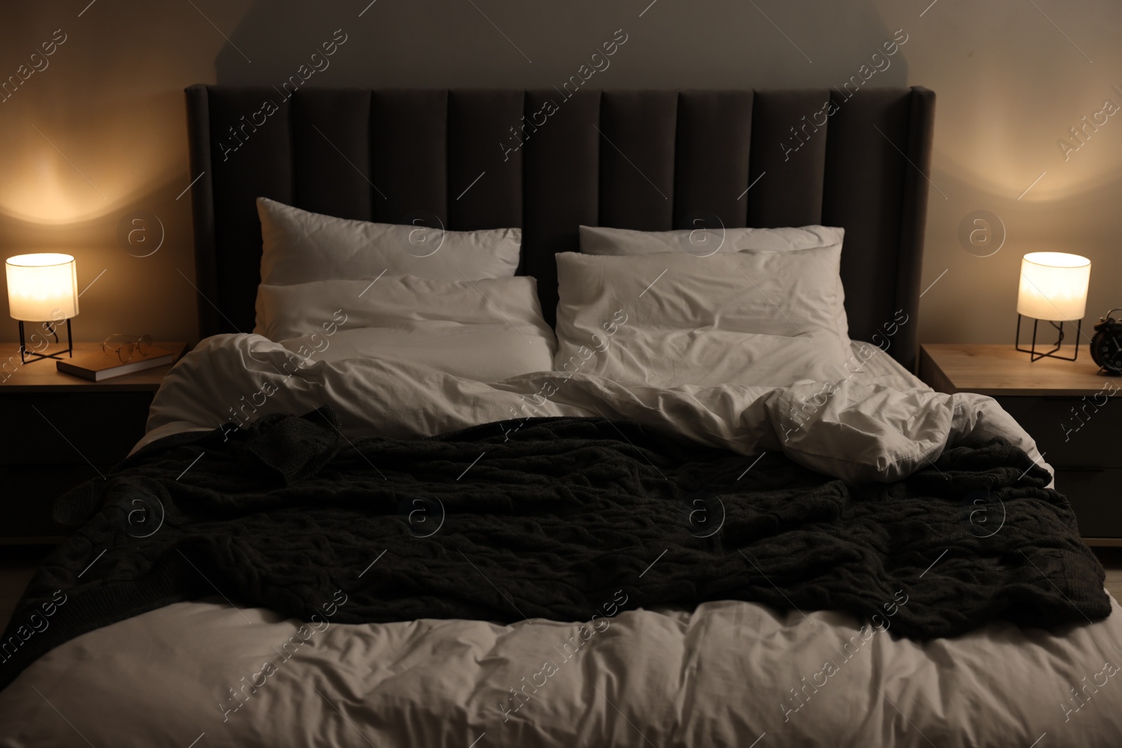 Photo of Large bed with pillows and duvet between nightstands indoors