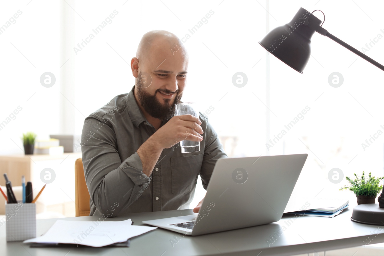 Photo of Portrait of confident young man with  laptop drinking water at table