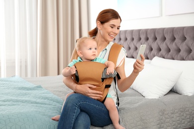 Photo of Woman with her son in baby carrier using smartphone at home