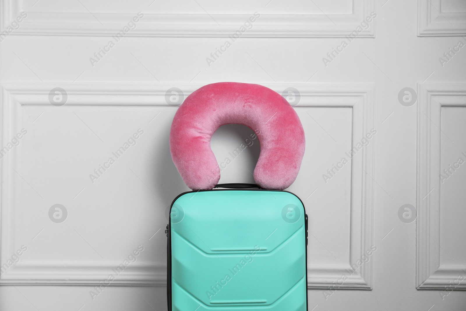 Photo of Pink travel pillow on turquoise suitcase near white wall