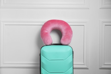 Pink travel pillow on turquoise suitcase near white wall