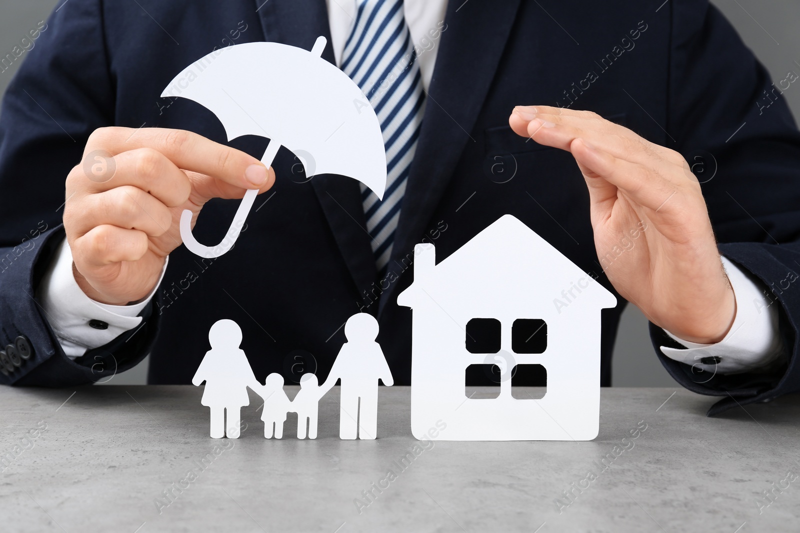 Photo of Man with cutout paper family, house and umbrella at table, closeup. Life insurance concept