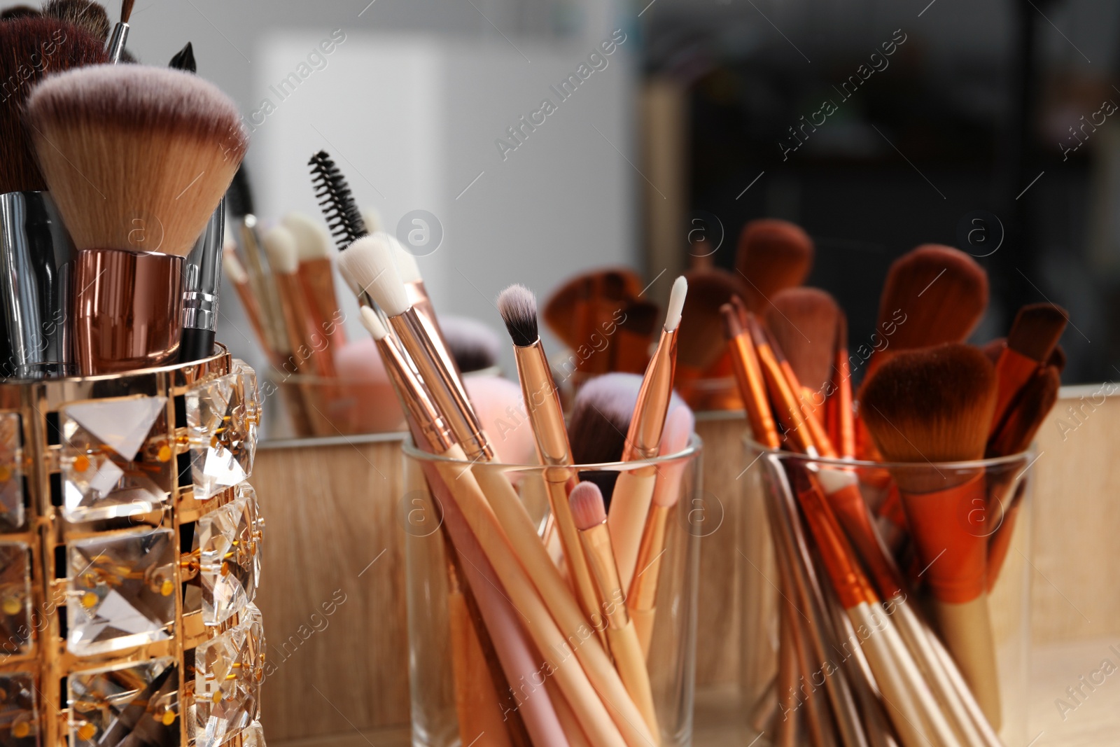 Photo of Set of professional makeup brushes near mirror on wooden table, closeup