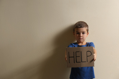 Little boy with sign HELP on yellow background, space for text. Child in danger