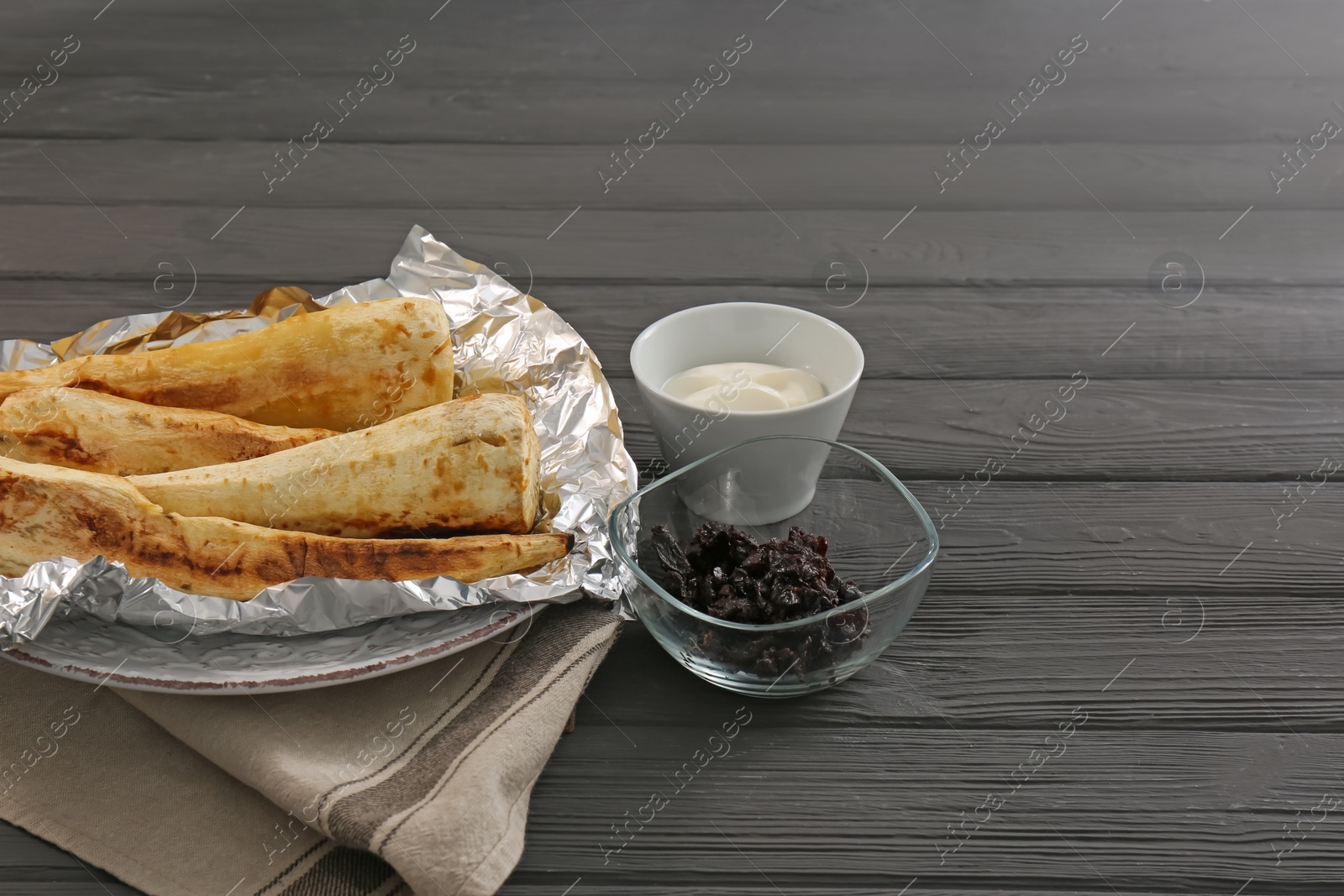 Photo of Tasty baked parsnips, prunes and sauce on dark wooden table. Space for text