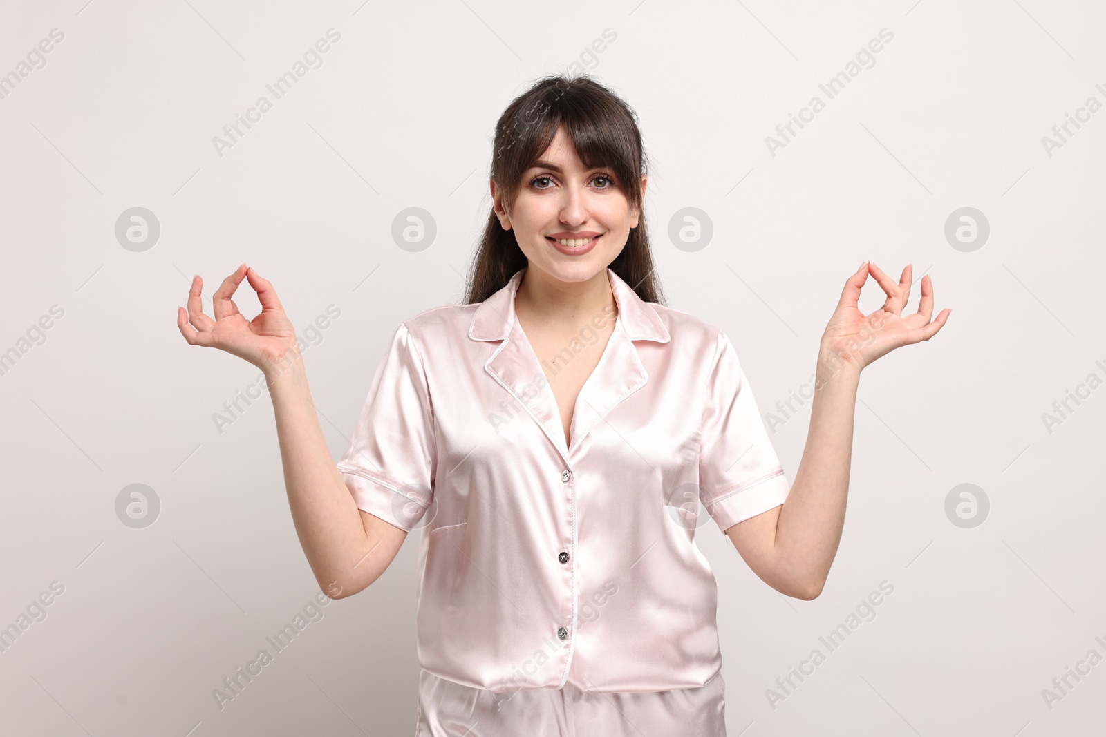 Photo of Woman in pyjama meditating on light grey background