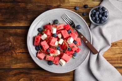 Photo of Delicious salad with watermelon, blueberries and feta cheese on wooden table, flat lay