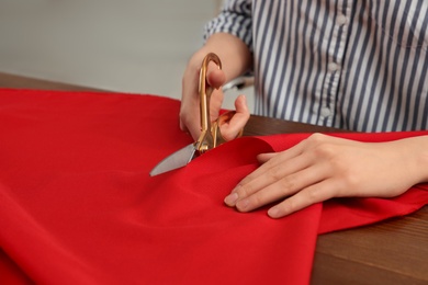 Photo of Woman cutting fabric with sharp scissors at wooden table, closeup. Space for text