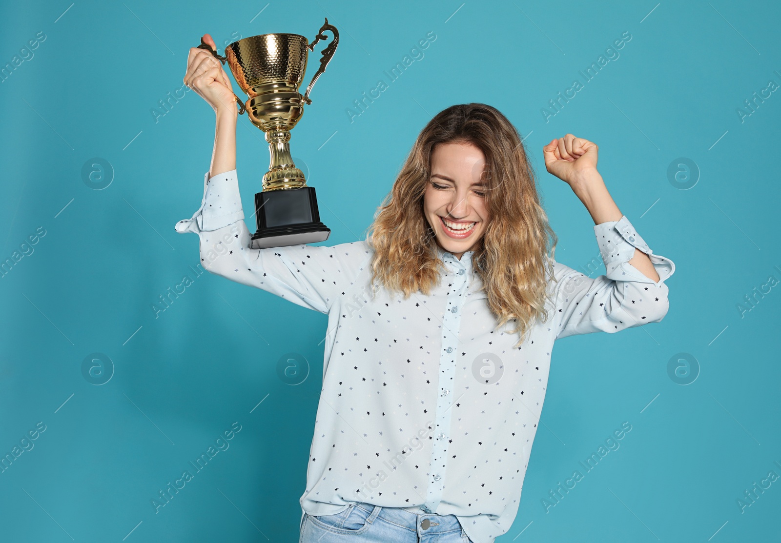 Photo of Portrait of happy young woman with gold trophy cup on blue background