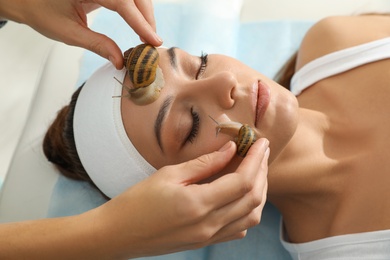 Photo of Young woman receiving snail facial massage in spa salon, closeup