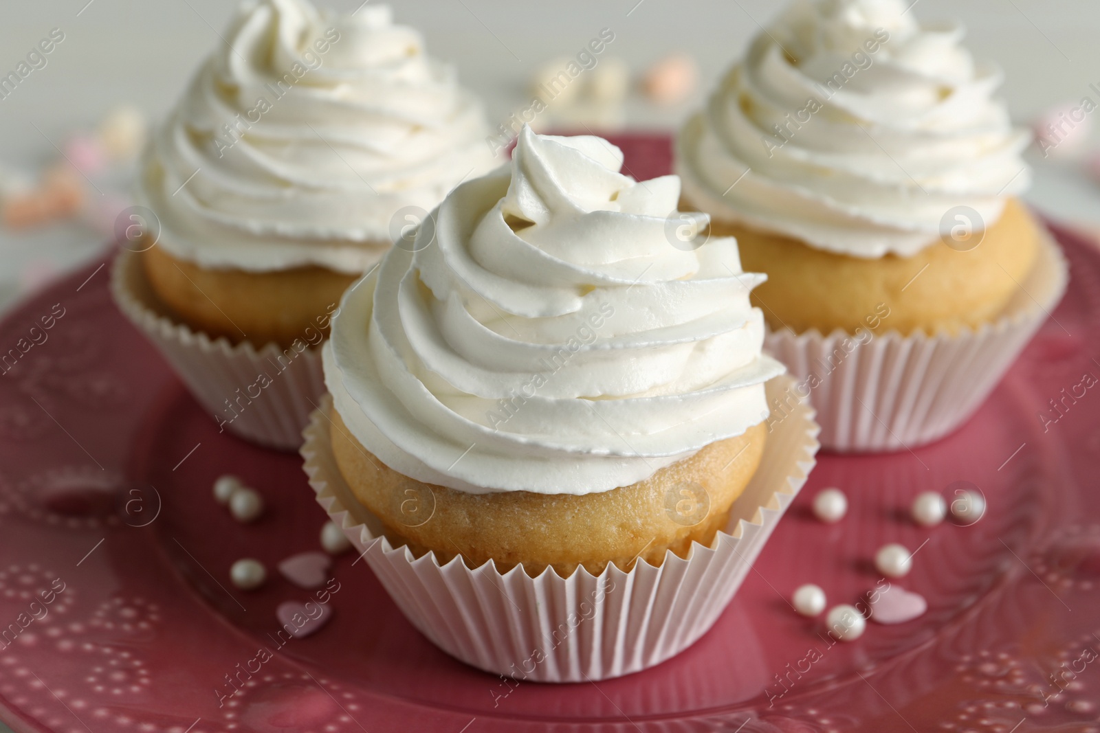 Photo of Delicious cupcakes with white cream on pink plate, closeup