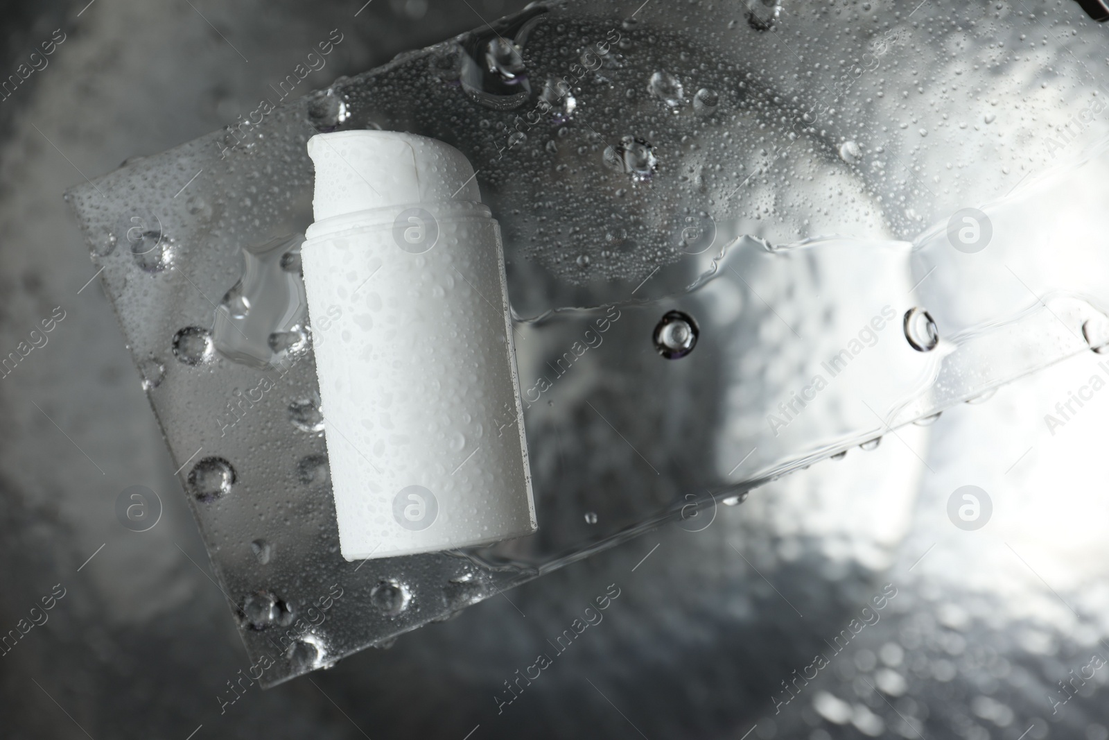 Photo of Moisturizing cream in bottle on glass with water drops against metal background, top view