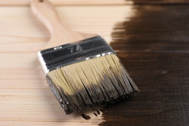 Photo of Brush with wood stain on wooden surface, closeup