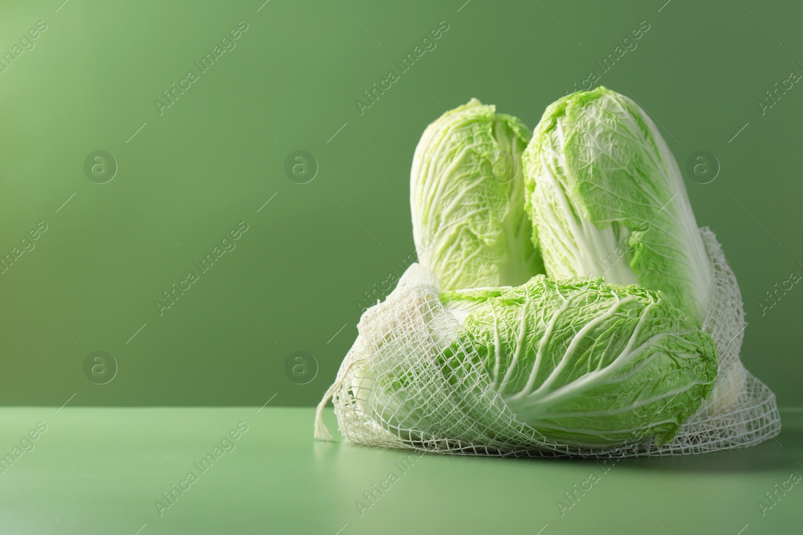 Photo of Fresh Chinese cabbages in string bag on green background. Space for text