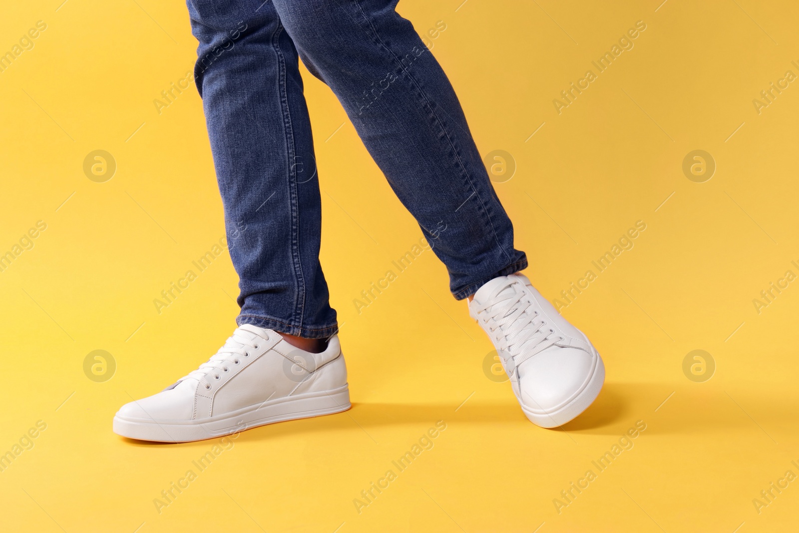 Photo of Man wearing stylish white sneakers on yellow background, closeup