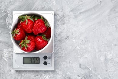 Kitchen scale with bowl of strawberries on grey textured table, top view. Space for text