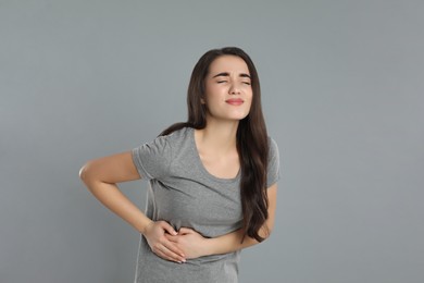 Young woman suffering from liver pain on grey background