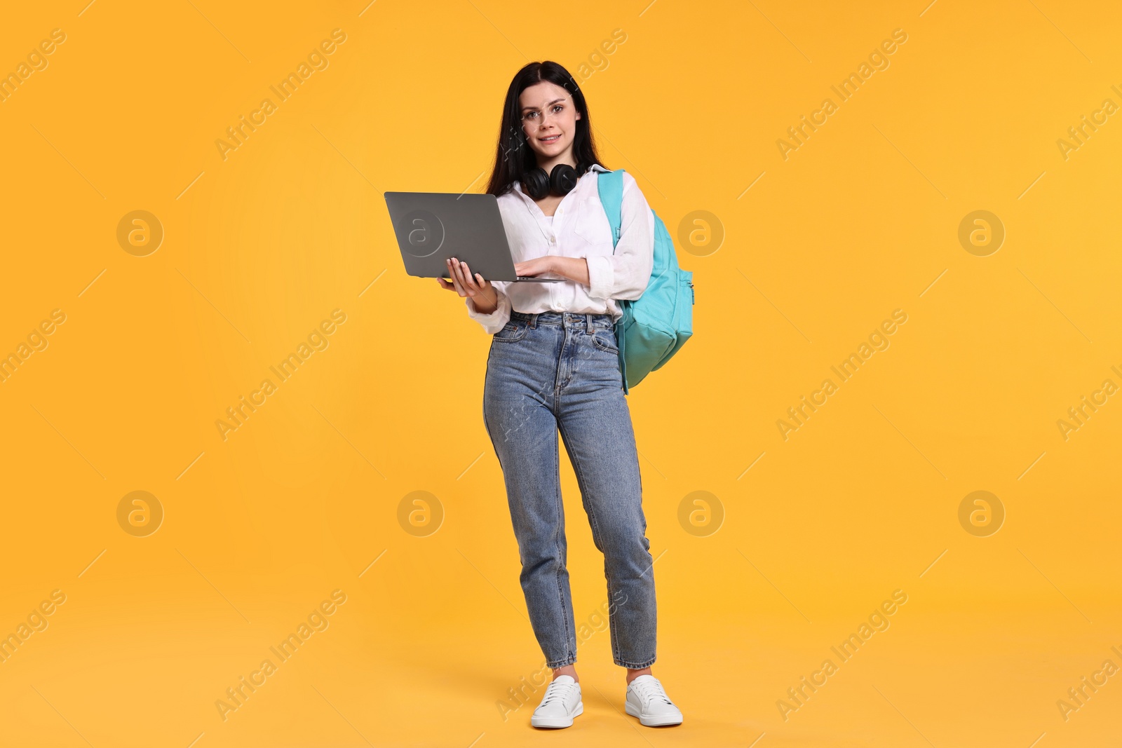 Photo of Smiling student with laptop on yellow background