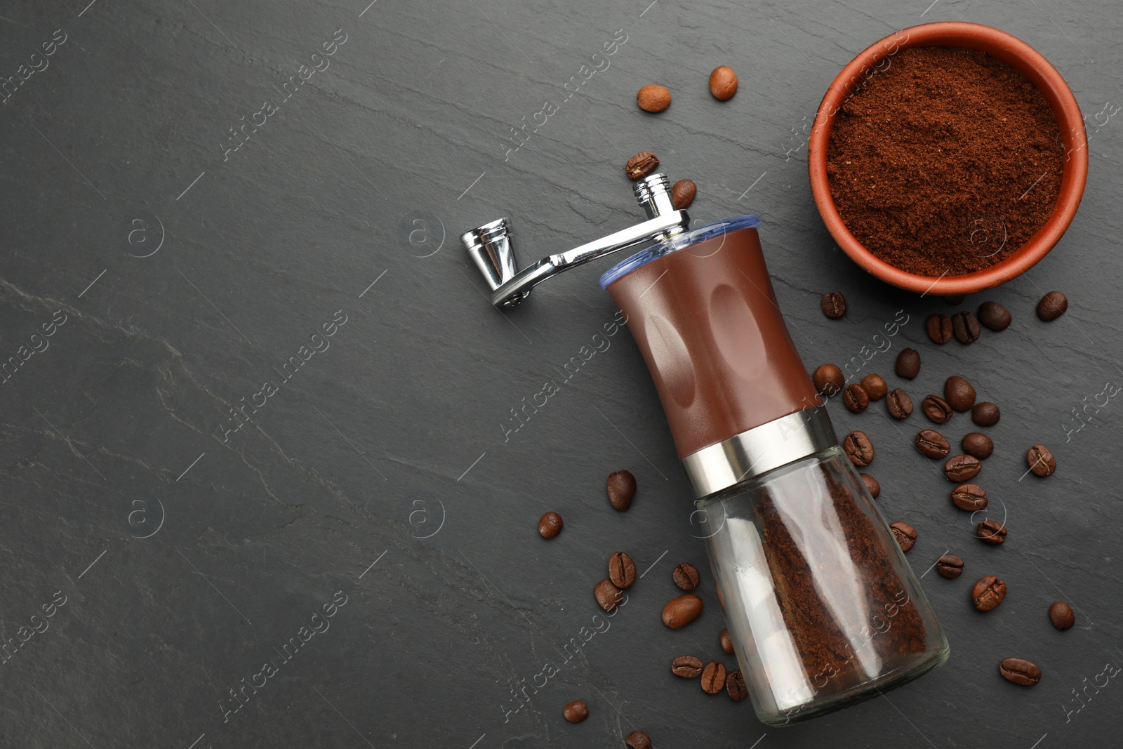 Photo of Modern manual coffee grinder with beans and powder on black table, flat lay. Space for text
