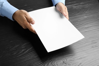 Photo of Man holding blank paper sheets for brochure at black wooden table. Mock up