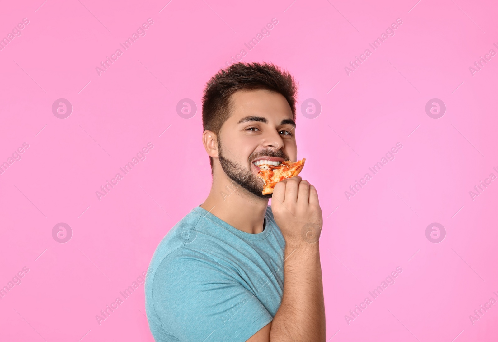 Photo of Handsome man eating pizza on pink background