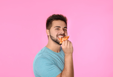 Handsome man eating pizza on pink background