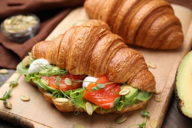 Photo of Tasty croissants with salmon, avocado, mozzarella and lettuce on wooden table, closeup