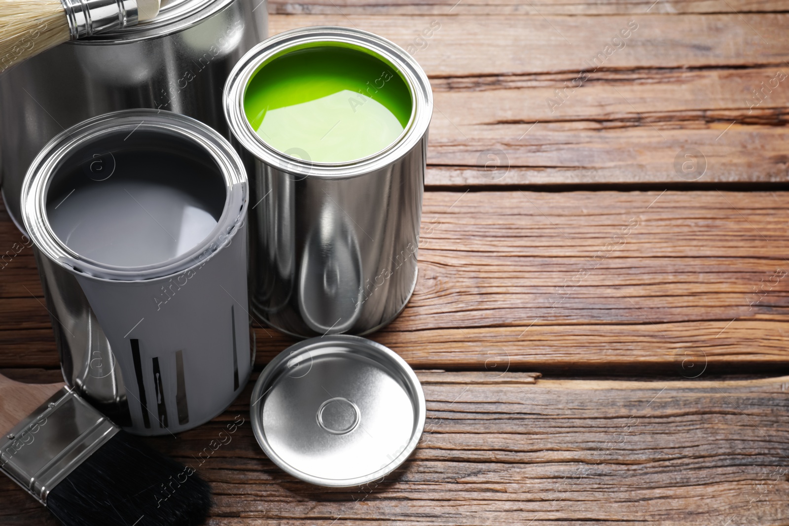 Photo of Cans of paints and brushes on wooden table, space for text