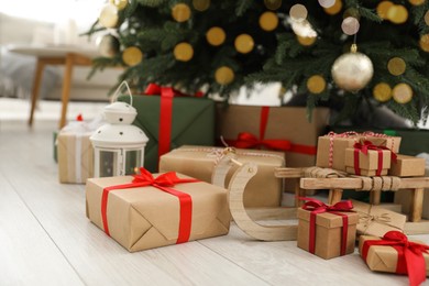 Beautifully wrapped gift boxes and wooden sleigh under Christmas tree indoors