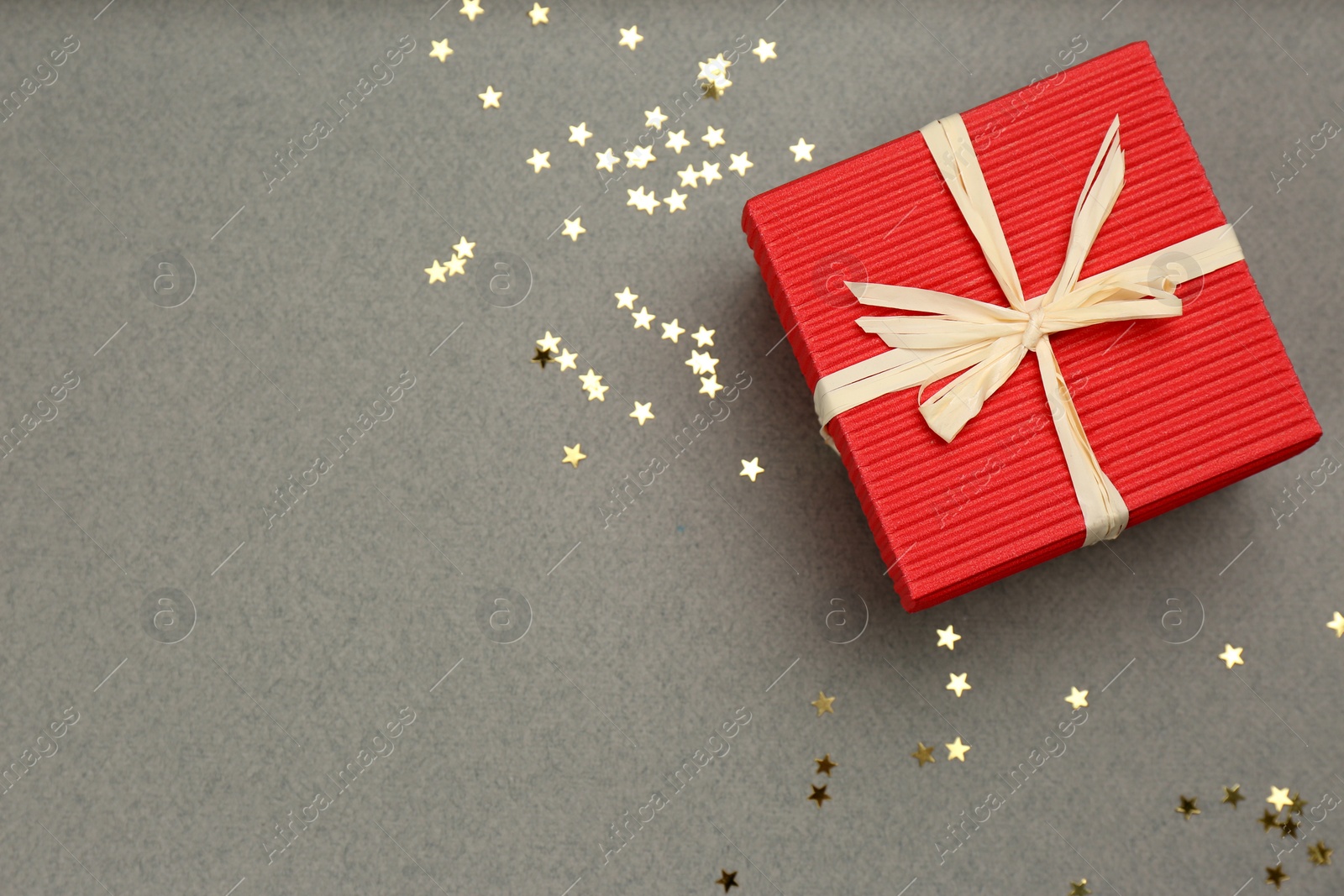 Photo of Red gift box and shiny confetti on grey background, top view. Space for text