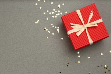 Photo of Red gift box and shiny confetti on grey background, top view. Space for text