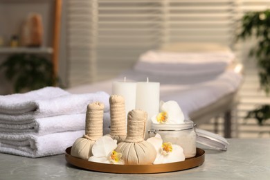 Photo of Tray with herbal bags, candles, scrub, beautiful flowers and folded towels on grey marble table in salon, space for text. Spa products