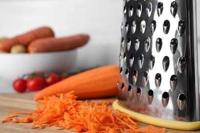 Photo of Grater and fresh ripe carrot on wooden board, closeup