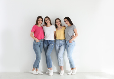 Photo of Beautiful young ladies in jeans and colorful t-shirts near white wall indoors. Woman's Day