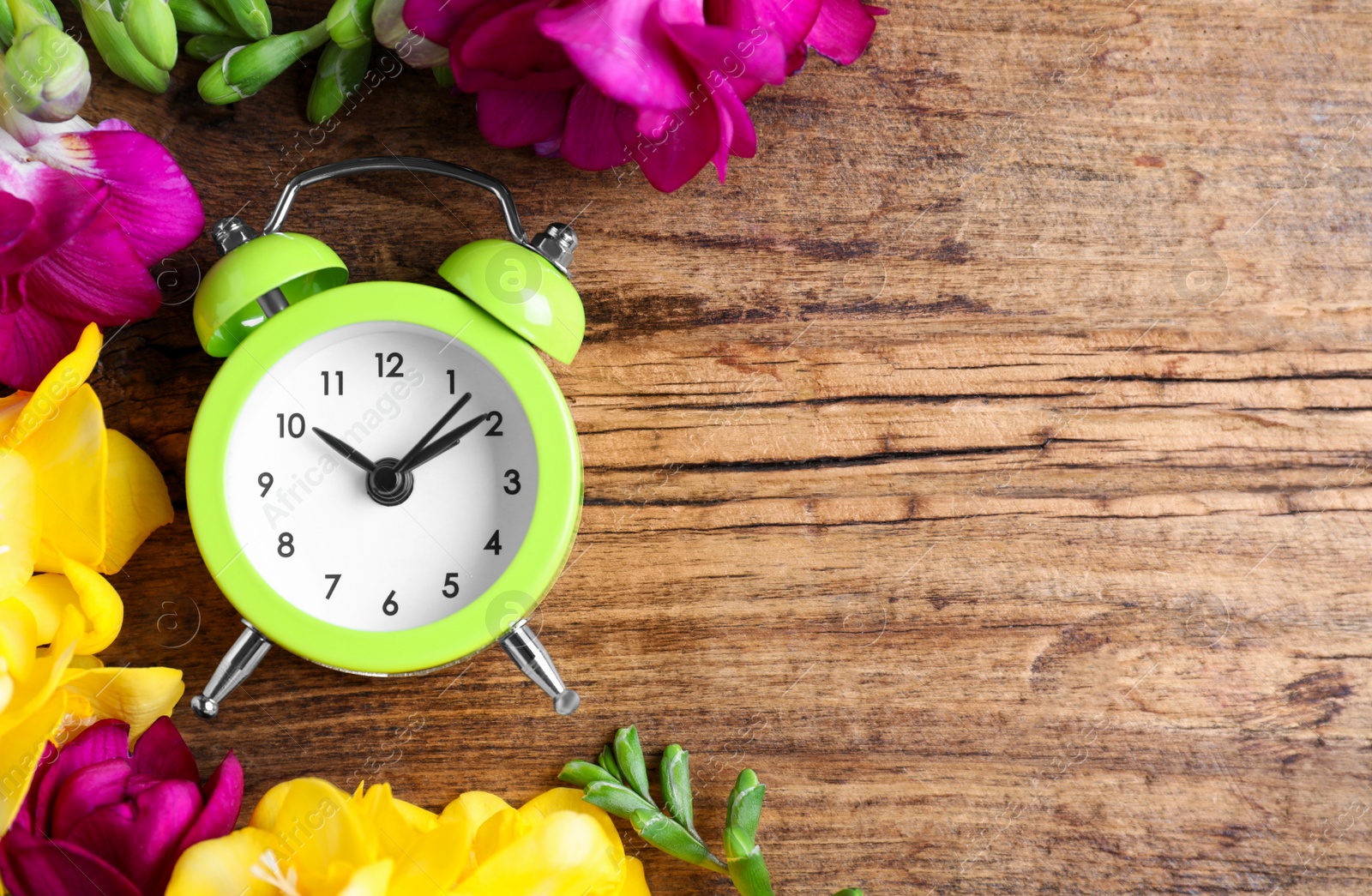 Photo of Green alarm clock with spring flowers and space for text on wooden table, flat lay. Time change