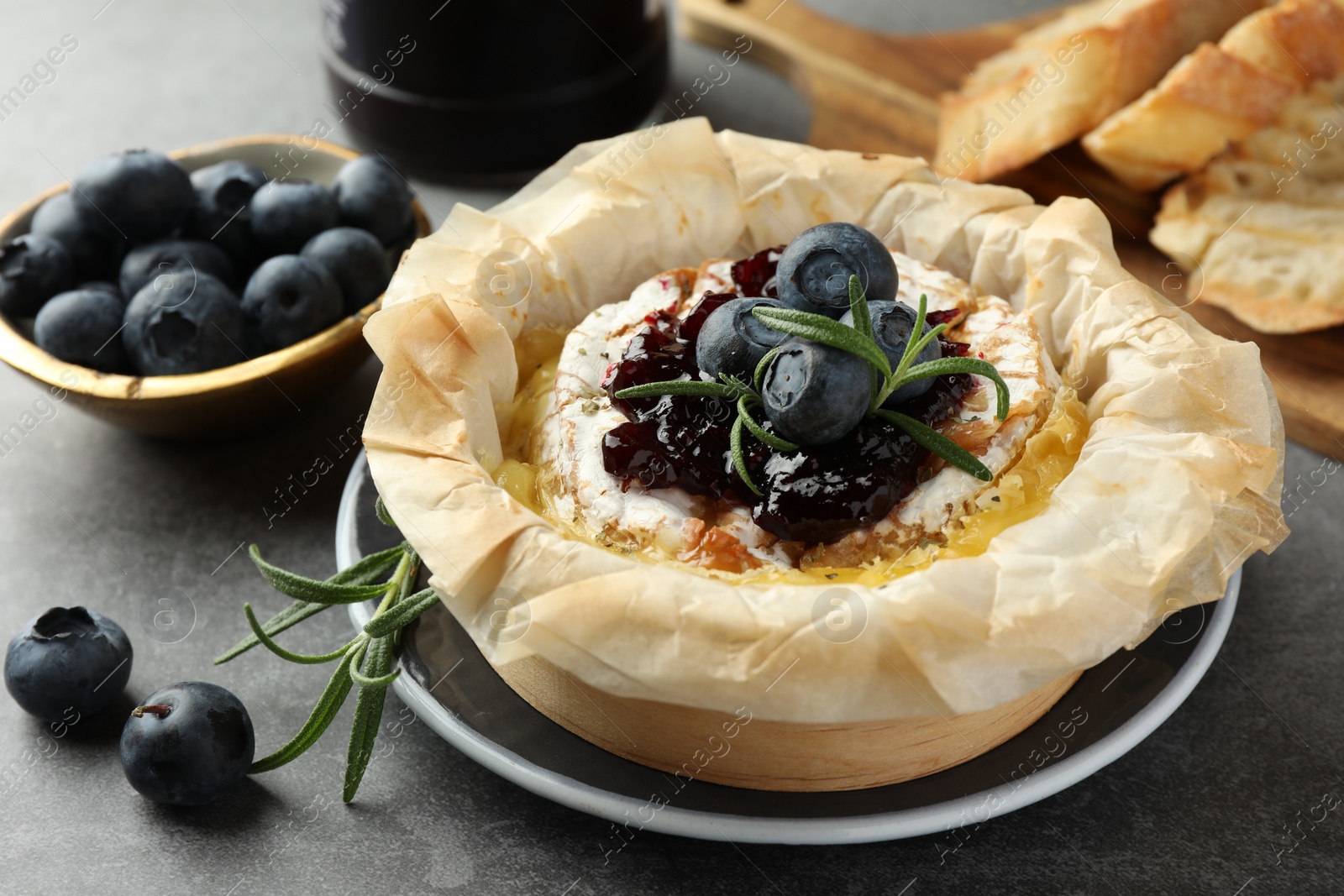 Photo of Tasty baked brie cheese with blueberries, jam and rosemary on grey table, closeup