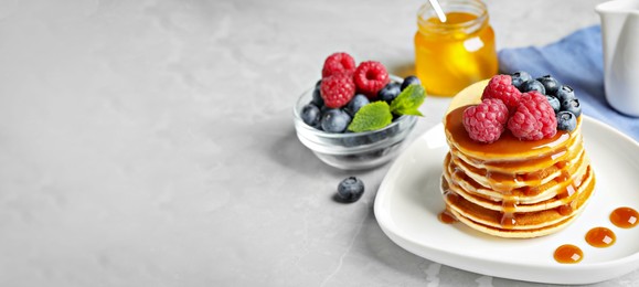 Image of Delicious pancakes with fresh berries and syrup on grey table, space for text. Banner design