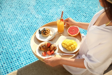 Young woman with delicious breakfast on tray near swimming pool, closeup