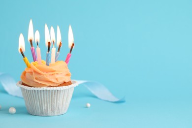 Photo of Tasty birthday cupcake with many candles on light blue background. Space for text